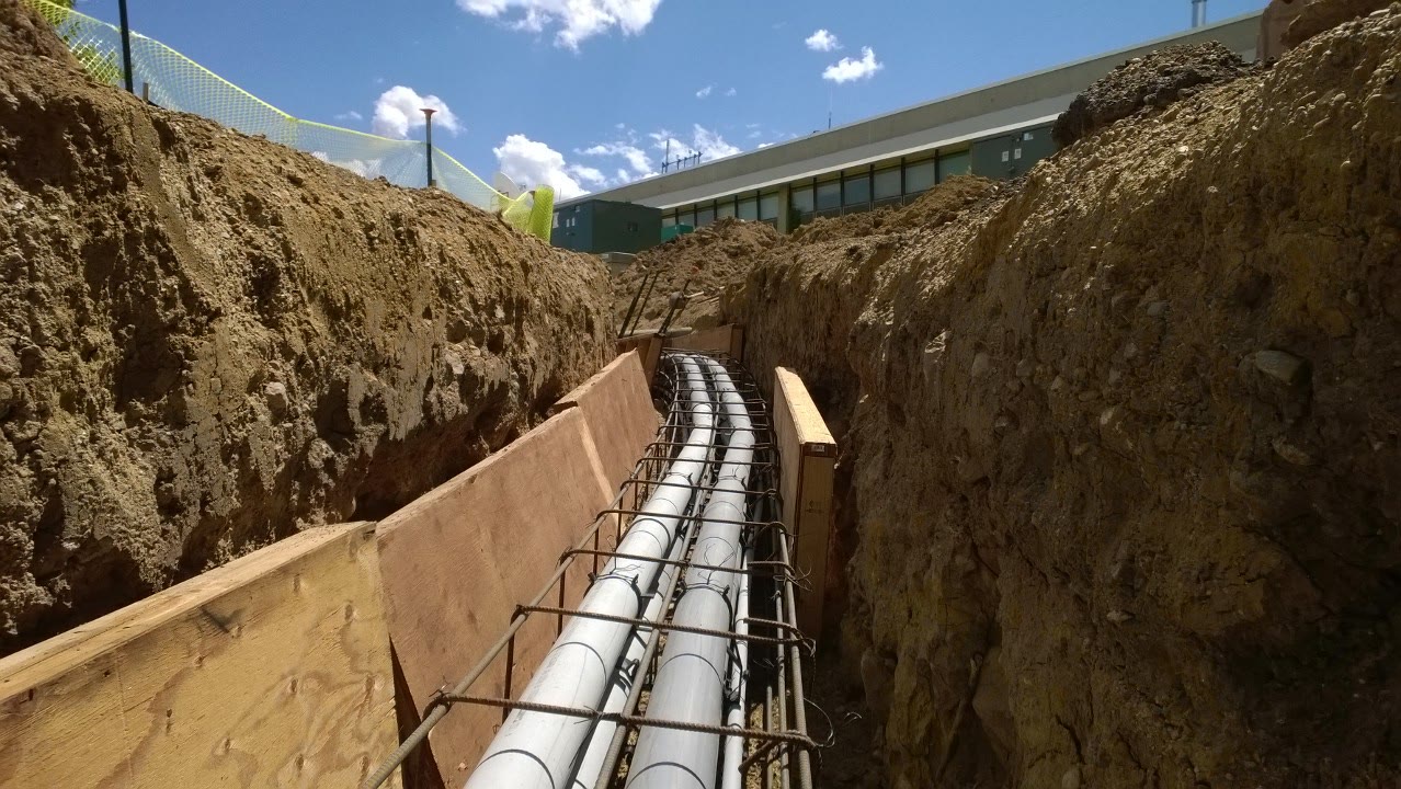 Gray conduit runs laid in a deep trench beside a commercial building